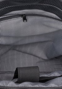 Wnętrze czarnego skórzanego plecaka wyłożone tkaniną w paski w odcieniach szarości i bieli. Wyposażone w kieszeń na zamek oraz zwinięty uchwyt z tkaniny.