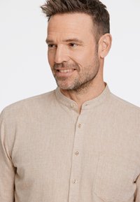 Lichtbeige lange mouwen shirt met een mandarin kraag, voorzien van kleine knopen en een borstzak. Getextureerde, geweven stof met een subtiel patroon.