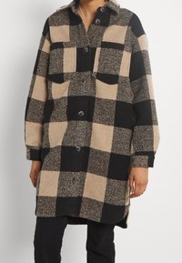 Rutig flanellskjorta i jackformat i svart och beige. Har en krage, två framfickor och knappar framtill. Mjuk textur.