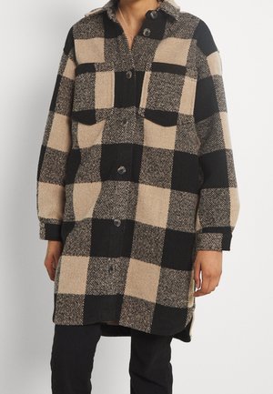 Chaqueta de franela a cuadros en negro y beige. Presenta un collar, dos bolsillos frontales y botones en el frente. Textura suave.
