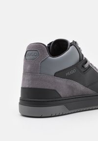 Harmaa korkea-ankainen tennari, jossa sileää nahkaa ja mokkanahkaa, kantapäässä brändäys sekä musta kumipohja, jossa pitourat.