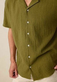 Korte mouw knoopshirt in olijfgroen, met een gemêleerde stof, kleine kraag en witte knopen aan de voorkant.