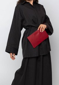 Black striped button-up shirt with wide sleeves, paired with a matching skirt, holding a red leather clutch with a logo embossed.