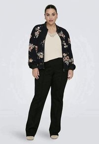 Corta-vento floral em azul marinho com detalhes em creme, combinado com uma blusa creme e calças pretas. Os sapatos são bege, apresentando um corte reto.