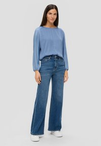 Hellbluse mit langen Ärmeln und entspannter Passform, kombiniert mit hochtaillierten, weiten Denim-Jeans. Weiße Sneakers vervollständigen das Outfit.