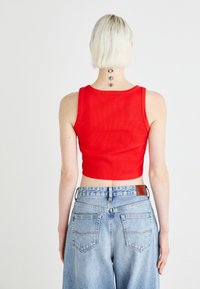 Röd ribbad kort topp i kombination med ljusblå hög midjejeans i denim, med bakfickor och en brun läderlapp på midjebandet.