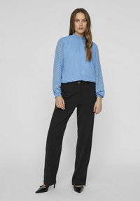 Blusa azzurro chiaro a maniche lunghe con un motivo a zigzag testurizzato e scollatura a ruches, abbinata a pantaloni neri a gamba dritta e tacchi a punta.