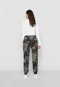 Camouflage Cargo-Hosen in Dunkelgrau und Schwarz mit elastischen Bündchen, Seitentaschen und einem lässigen Schnitt, kombiniert mit einem weißen Langarmoberteil.