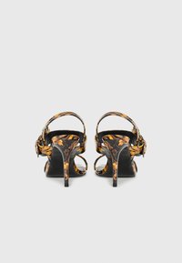Sandálias de salto alto com um padrão floral em preto e dourado, design de ponta aberta e tiras no tornozelo. O salto stiletto tem aproximadamente 10 cm de altura.