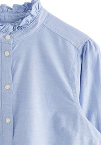 Lichtblauwe overhem shirt met een gerimpelde kraag, gemaakt van zachte stof. Beschikt over een knoopsluiting met zes witte knopen enGathered mouwen.