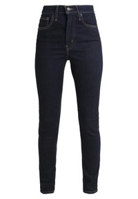 Jeans de cinta alta em azul escuro, feitos de denim. Apresentam um silhueta ajustada, bolsos frontais e costuras contrastantes ao longo das costuras.