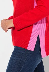 Rood en roze kleurgebroken trui met ribbeltextuur, voorzien van zijsplitsen en lange mouwen. Breigaren materiaal, casual ontwerp.