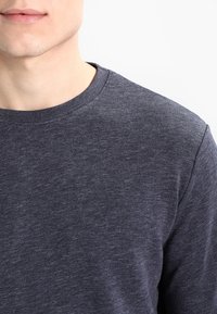 Ciemnoszary sweter z okrągłym dekoltem wykonany z teksturowanej tkaniny, prezentujący prosty fason z prążkowanym wykończeniem dekoltu i długimi rękawami.