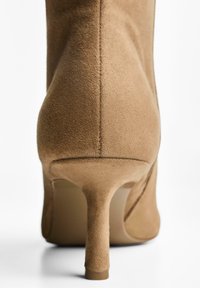 Cizmă stiletto din suede bej cu vârf ascuțit, având o textură netedă și o formă elegantă, accentuând un toc subțire și conic.