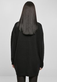 Black oversized sweater with a textured finish, dropped shoulders, and a loose fit, extending to mid-thigh, paired with patterned leggings.
