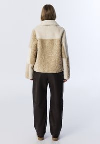 Crème en beige textuurjacket met een kraag, met een blokpatroon. Gedragen met donkerbruine geplooide broeken en platte schoenen.