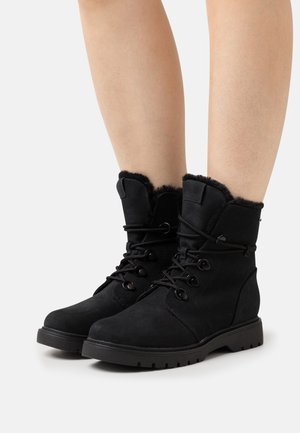 Bottes bottines en suède noir avec doublure en fourrure, devant à lacets et semelle en caoutchouc. Caractéristiques : bout rond et boutons décoratifs sur le côté.