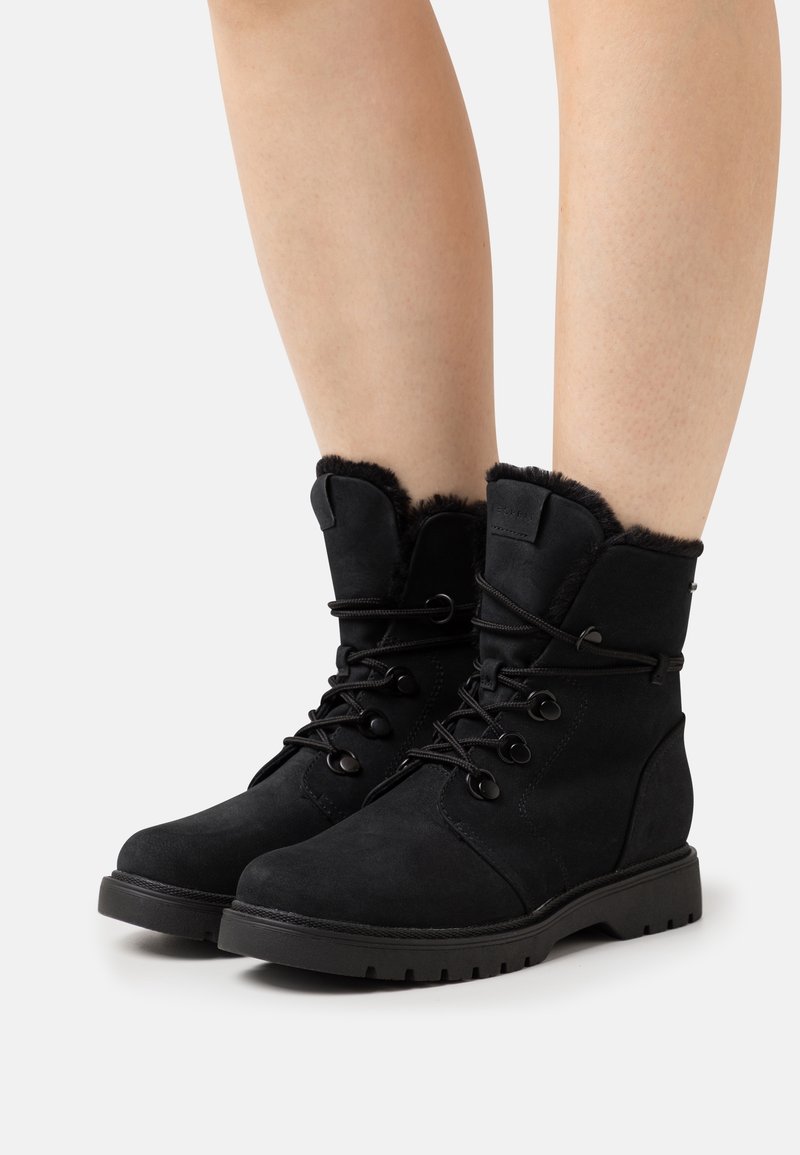Bottes bottines en suède noir avec doublure en fourrure, devant à lacets et semelle en caoutchouc. Caractéristiques : bout rond et boutons décoratifs sur le côté.
