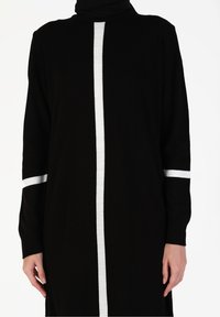 Robe en tricot noir avec une rayure blanche centrale et des accents blancs sur les manches. Le design a une coupe décontractée avec un col montant.