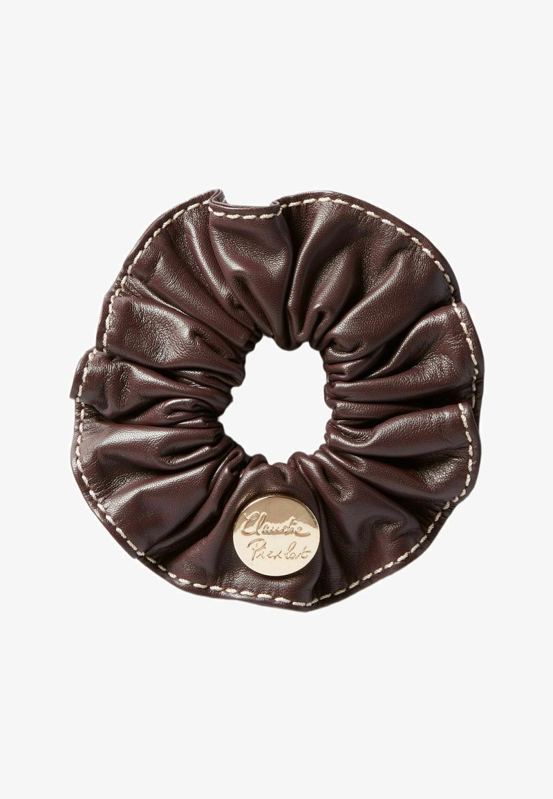 Gomita de cuero marrón con textura arrugada y costura crema. Presenta una placa de logotipo dorada para la identificación de la marca. Forma redonda.