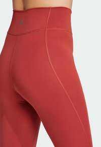 Czerwone legginsy z wysokim stanem, wykonane z elastycznego materiału, z płaskimi szwami i subtelnym detalem logo na talii dla dodatkowego designu.