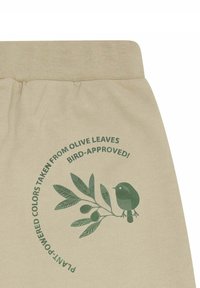 Beige stof met een gestructureerde tailleband, gekenmerkt door een groen, rond ontwerp van een olijftak en vogel, met het label "plantenkrachtige kleuren afgeleid van olijf bladeren."