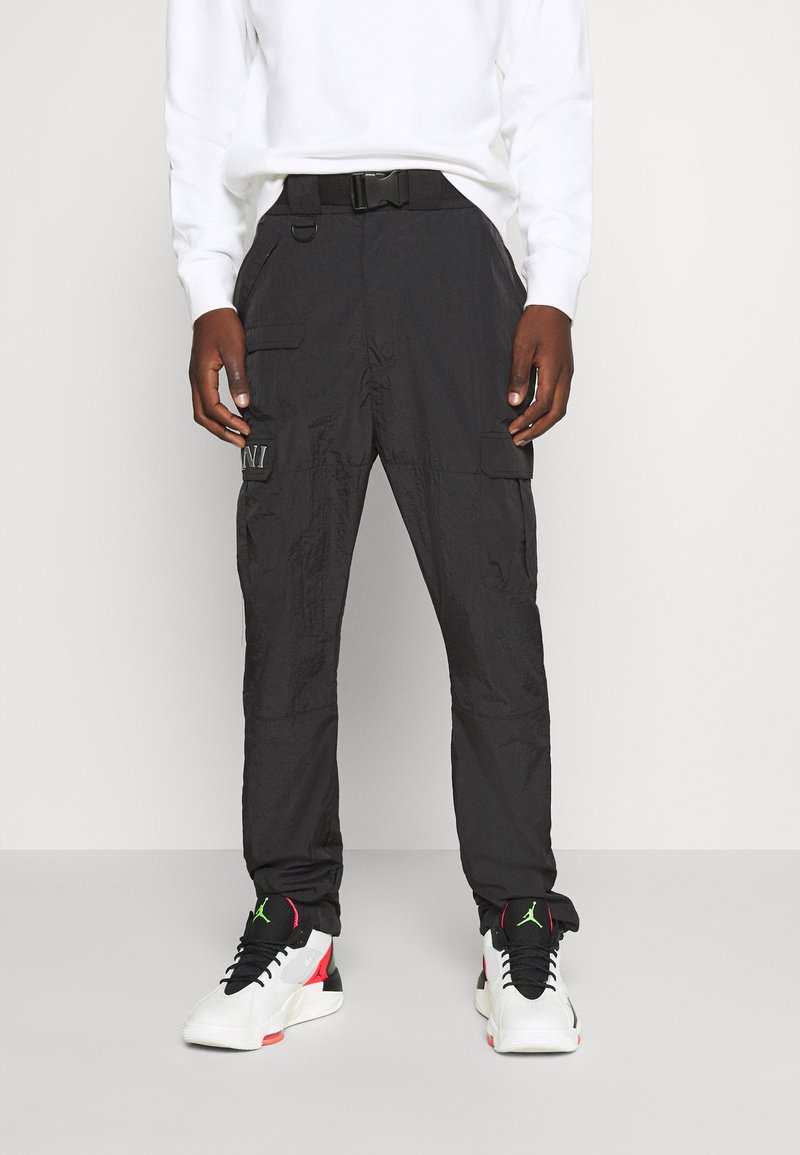 Personne portant un pantalon cargo noir avec plusieurs poches et une ceinture, associé à des baskets montantes blanches, noires, rouges et vertes.