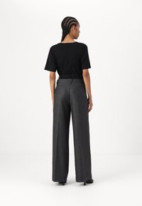 Un tricou negru scurt, asortat cu pantaloni larghi în talie înaltă, gri închis, cu un model discret de carouri și buzunare pe spate.