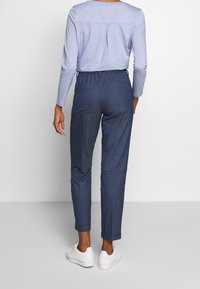 Haut bleu clair à manches longues avec un col rond, associé à un pantalon bleu foncé fuselé avec une taille élastique et des revers roulés. Baskets blanches.