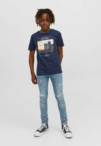 Mørkeblå bomull t-skjorte med trykk på forsiden, paret med lysebl�å slitte jeans og mørke sneakers med hvite såler.