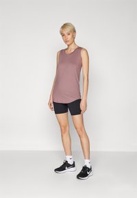 Ujjatlan világos mályva színű tank top, fekete rövidnadrág, fekete sportcipő fehér díszítéssel és fehér zokni. Sima anyag, laza szabás, minimális részletezés.