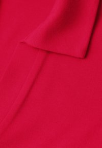Tissu rouge vif avec un col plié et un détail de couture visible, montrant une texture lisse et tissée serrée.