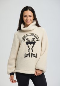 Cremfarbener Fleece-Pullover mit hohem Kragen, der schwarze grafische Designs umfasst, darunter ein rentiermotiv und geometrische Akzente auf der Vorderseite.
