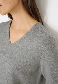 Grau V-Ausschnitt Pullover aus weichem Strickmaterial, mit gerippten Akzenten am Ausschnitt und an den Schultern. Glatte Textur mit subtiler Musterung.