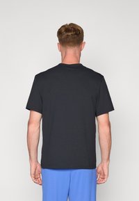 Camiseta de algodón negra con mangas cortas y cuello redondo, con un diseño liso y un corte regular, vista desde la espalda.