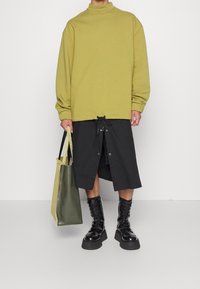 Felpa oversize verde oliva, gonna nera al ginocchio con bottoni e stivaletti platform neri. Abbinata a una borsa a tracolla verde.