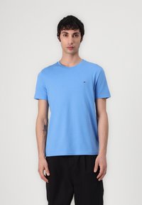 Kurzärmliges T-Shirt mit Rundhalsausschnitt aus leichtem blauen Baumwollstoff, das ein kleines Logo auf der linken Brust und eine glatte Textur aufweist.
