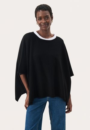 Pullover nero oversize con colletto a girocollo bianco, caratterizzato da maniche corte e una consistenza morbida, abbinato a jeans in denim blu.