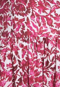 Motif abstrait de feuilles rouges et roses sur tissu blanc avec un détail de couture froncée au centre.