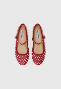 Zapatos planos rojos con un diseño de punta redonda, adornados con tachuelas plateadas y una correa decorativa a lo largo del empeine.