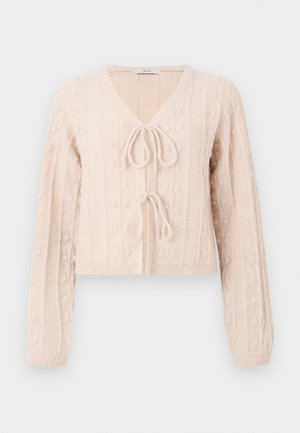 Cardigan court rose clair en tissu tricoté texturé, avec un décolleté en V et une fermeture à nouer à l'avant. Accentuée par des motifs en relief verticaux.