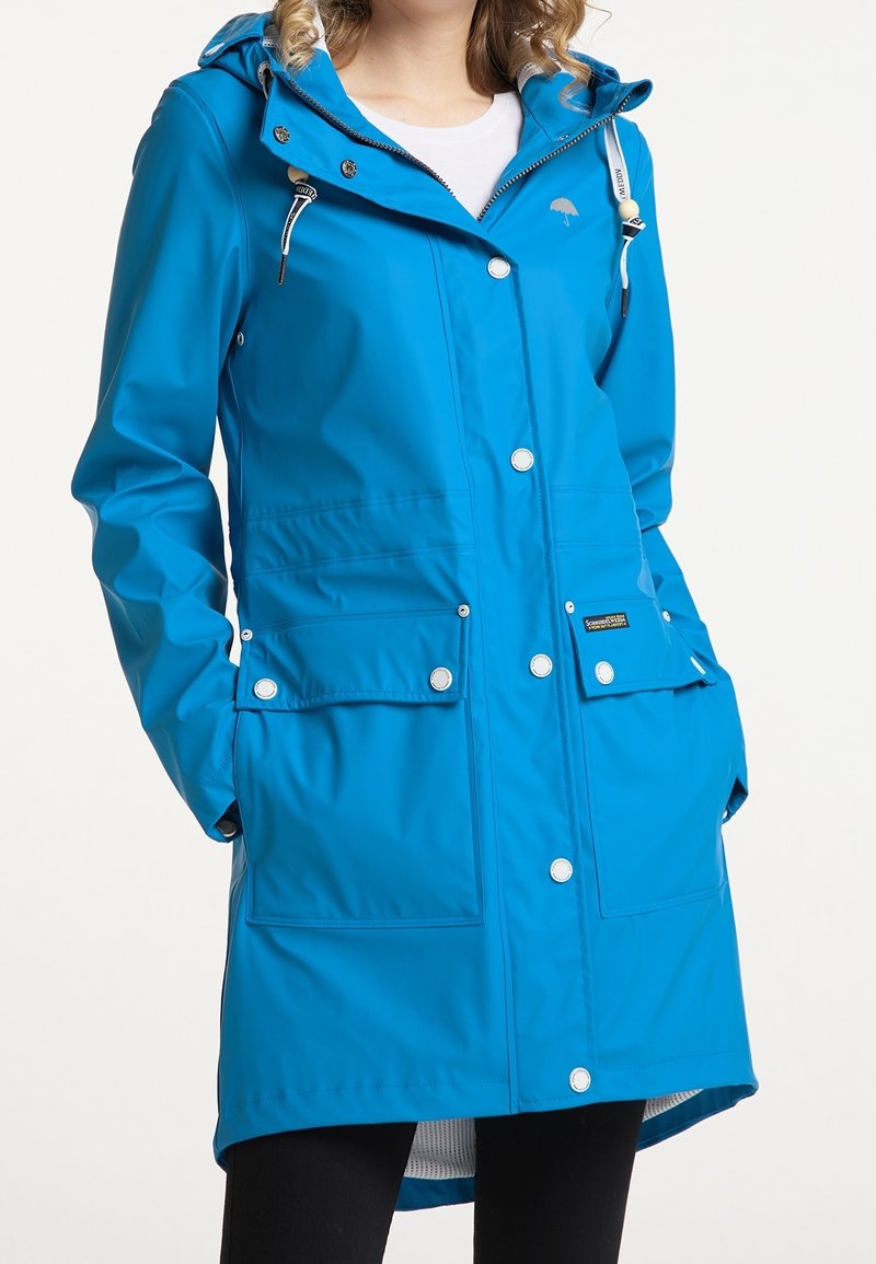 Modrá voděodolná pláštěnka s kapucí, snapovými knoflíky a dvěma předními kapsami. Vyrobena z hladkého materiálu s střední délkou a s možností nastavení.
