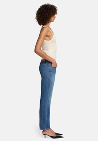 Jeans in denim blu con taglio dritto, dotati di tasche posteriori. Abbinati a un top aderente a costine color crema e a un paio di décolleté nere.