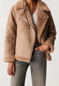 Brown faux shearling jacket with a notched collar, zipper closure, and soft texture; features fur-lined cuffs and a relaxed fit.