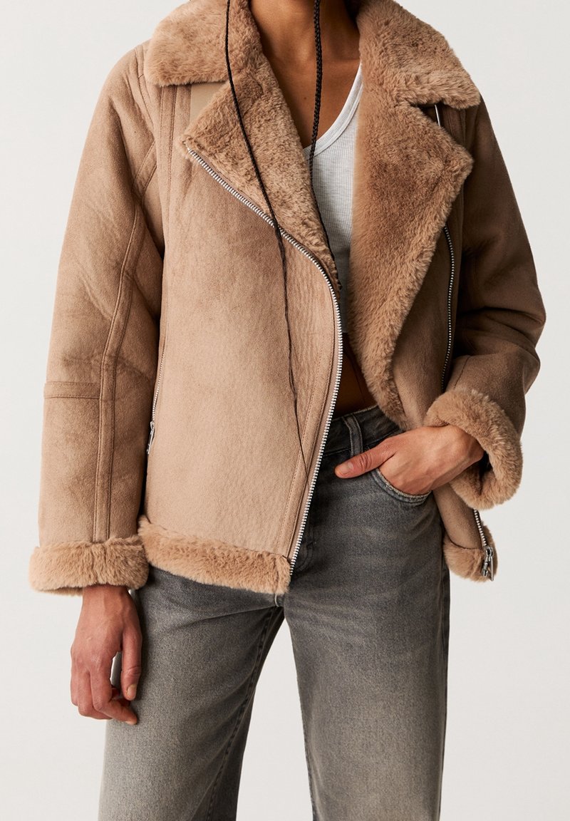 Brown faux shearling jacket with a notched collar, zipper closure, and soft texture; features fur-lined cuffs and a relaxed fit.