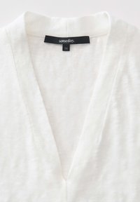 Top bianco, leggero, con scollo a V e una texture morbida, con un'etichetta che dice "un giorno." Taglia "36" visibile all'escollatura.