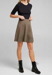 Zwarte top met korte mouwen gecombineerd met een bruin geruite A-lijnrok en zwarte veterschoenen tot de enkels, met een gladde textuur en een knielange uitstraling.