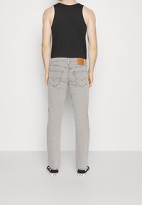 Jeans de mezclilla gris con corte recto, que presentan una etiqueta de cuero en la parte trasera de la cintura y dos bolsillos traseros con detalles de costura.