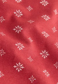 Roter Stoff mit einem strukturierten Strickdesign, das weiße Schneeflockenmuster in verschiedenen Größen auf gleichmäßige Weise über die Oberfläche verteilt zeigt.