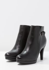 Schwarze Knöchelstiefel aus glänzendem Leder mit runder Zehenpartie, hohem Absatz und Schnallenverzierung an der Seite. Reißverschluss auf der Rückseite.